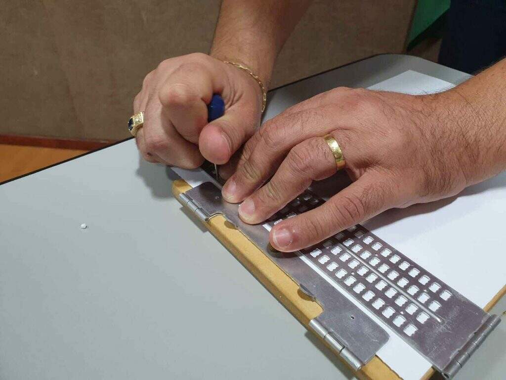 Mãos com equipamento e punção para escrever em braille 
